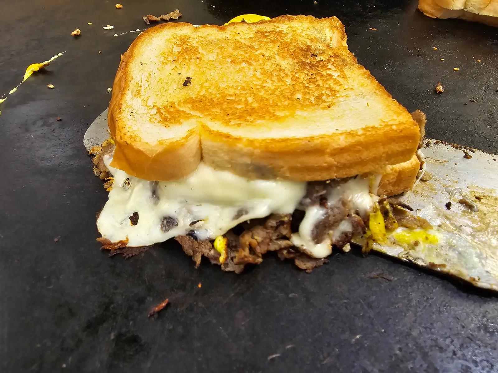 Cheesesteak grilled cheese with melted white cheese on the food truck griddle