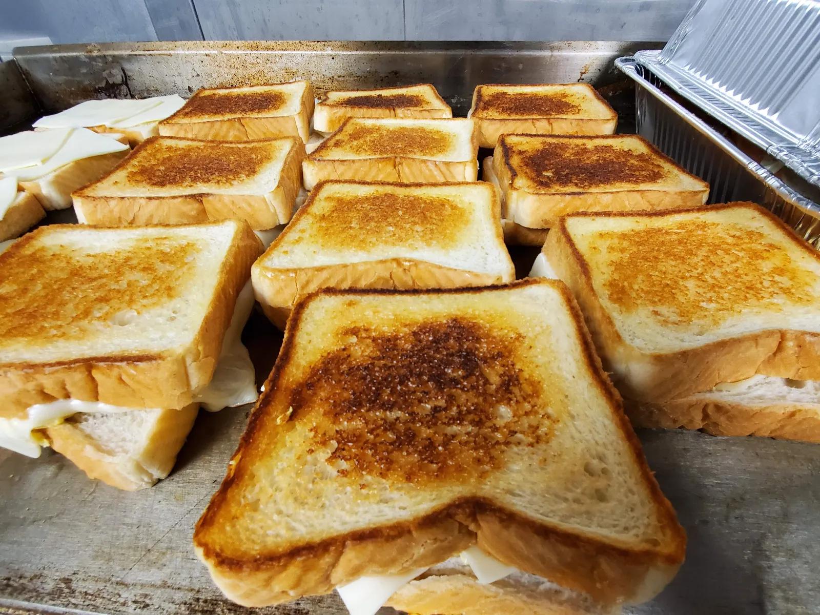 Rows of golden grilled cheese sandwiches on the Grilly Cheese food truck flat-top griddle