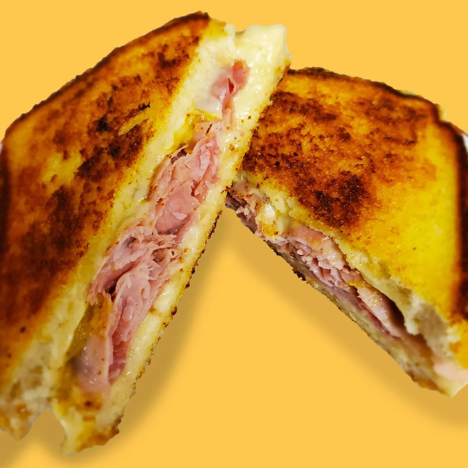 Ham and Swiss grilled cheese cut in half, stacked with sliced ham and melted Swiss cheese