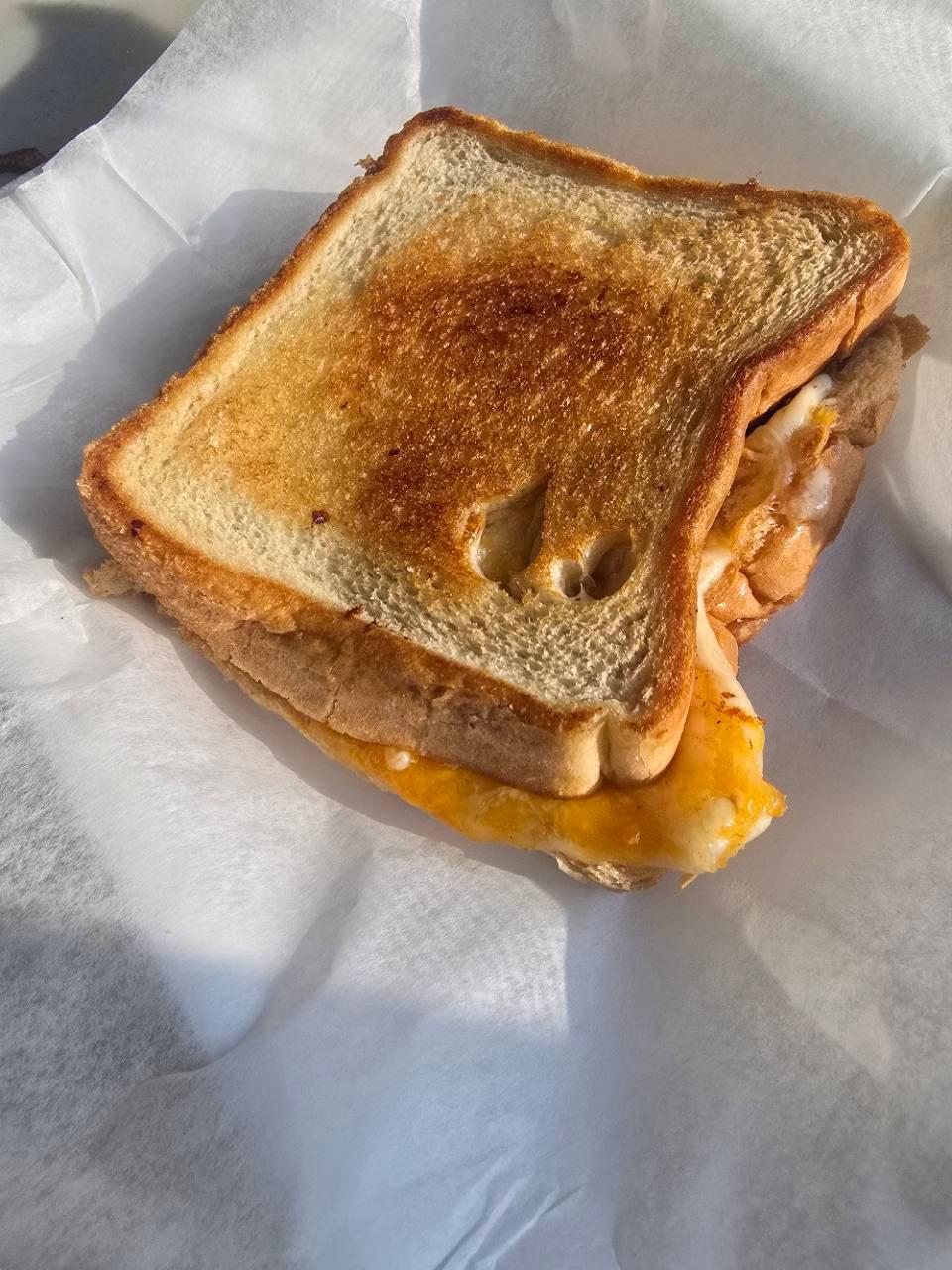 A toasted Grilly Cheese sandwich with melted cheese on deli paper